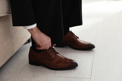 Photo of Groom putting on elegant wedding shoes indoors, closeup