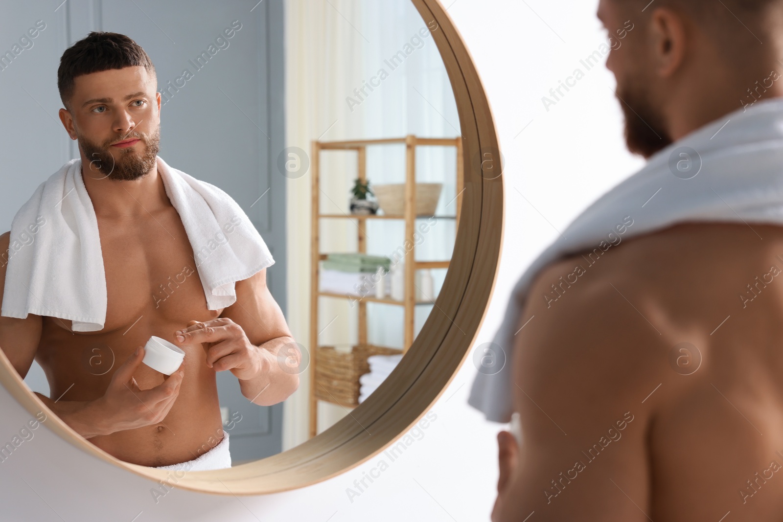 Photo of Handsome man applying body cream near mirror in bathroom