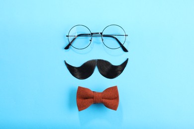 Photo of Artificial moustache, bowtie and glasses on light blue background, flat lay