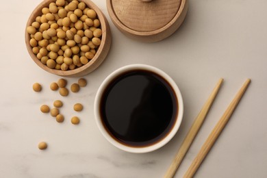 Soy sauce in bowl, soybeans and chopsticks on white marble table, flat lay