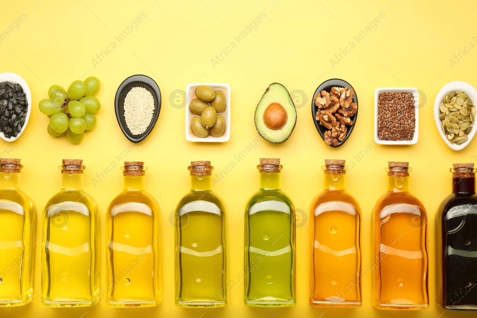 Photo of Vegetable fats. Different oils in glass bottles and ingredients on yellow table, flat lay