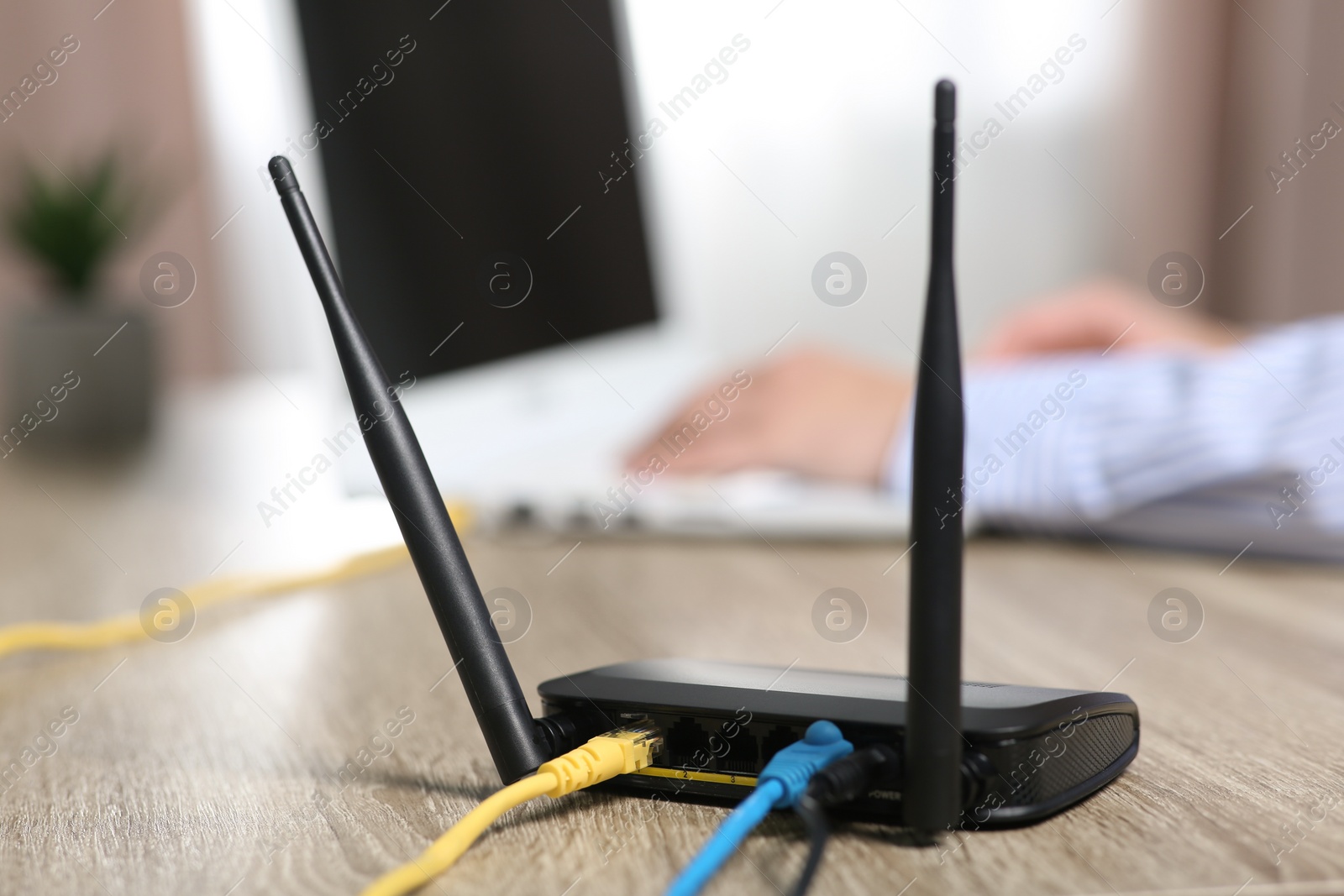 Photo of Woman working with laptop at table indoors, focus on Wi-Fi router