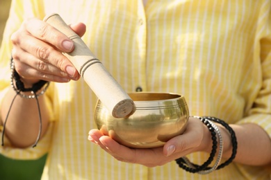 Photo of Woman using singing bowl in sound healing therapy outdoors, closeup