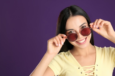 Beautiful woman wearing sunglasses on purple background. Space for text