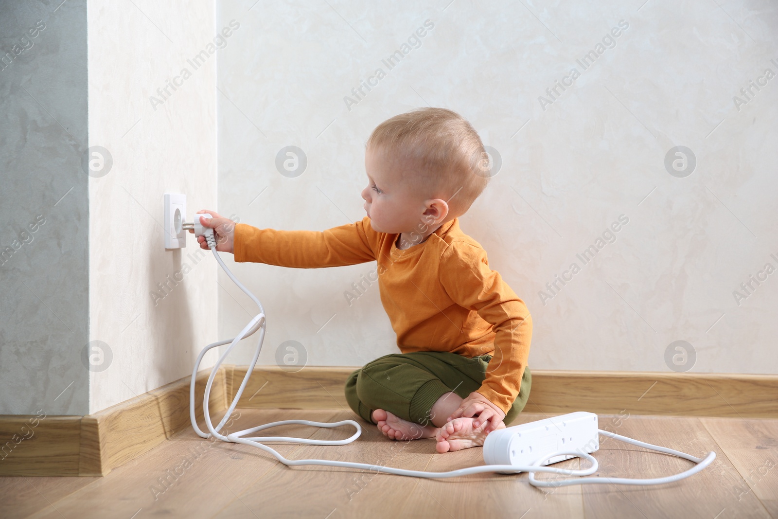 Photo of Little child playing with electrical socket and power strip plug at home. Dangerous situation