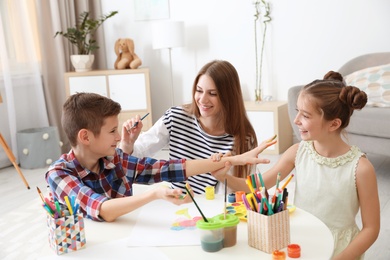 Photo of Young woman and children having fun with paints at table indoors
