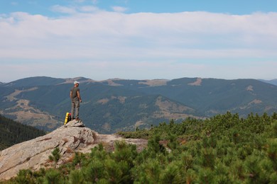 Photo of Man with backpack on rocky peak in mountains, back view
