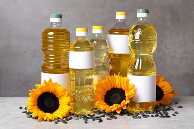 Bottles of sunflower cooking oil, seeds and yellow flowers on light grey table
