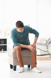 Photo of Young man suffering from knee pain at home