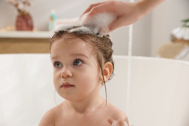 Photo of Mother washing her little daughter`s hair with shampoo in bathroom, closeup