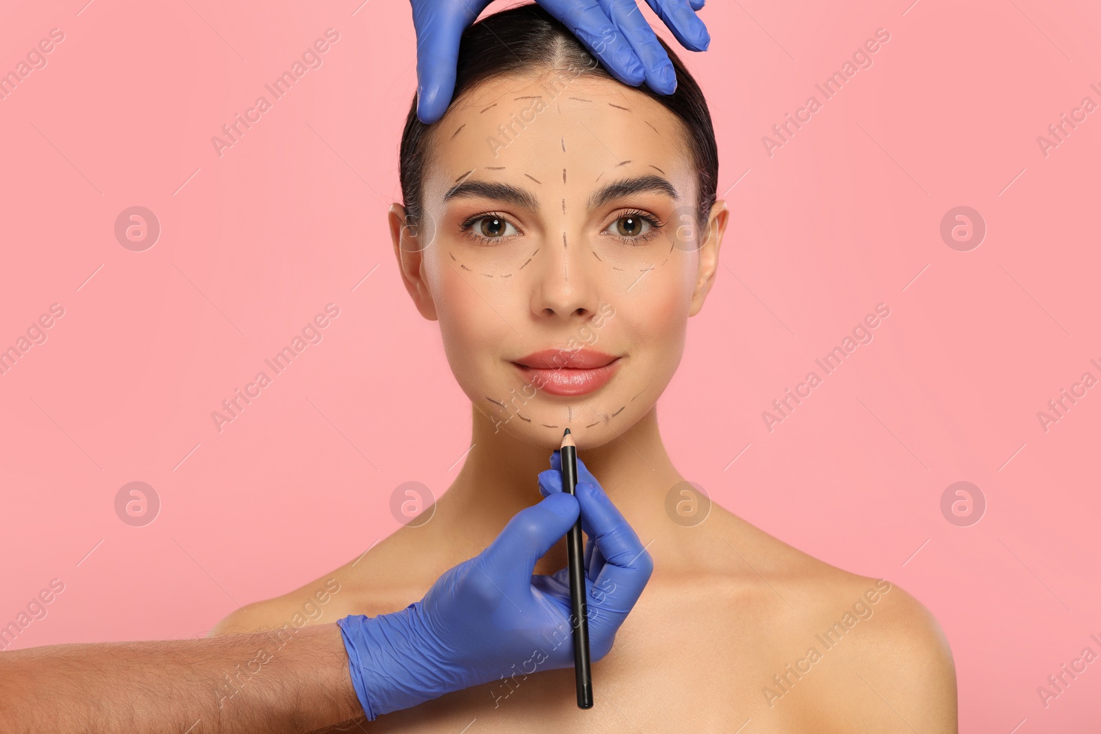 Photo of Doctor with pencil preparing patient for cosmetic surgery operation on pink background