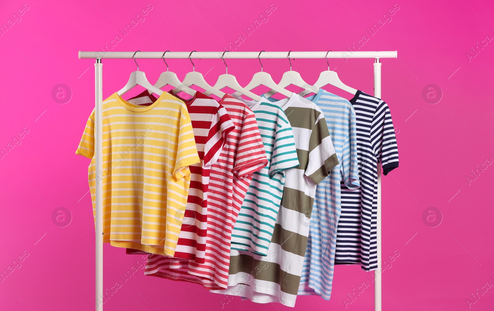 Photo of Colorful clothes hanging on rack against pink background