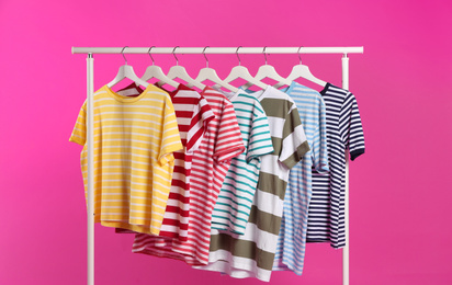 Photo of Colorful clothes hanging on rack against pink background