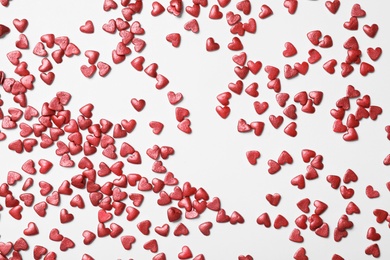 Photo of Bright heart shaped sprinkles on white background, flat lay