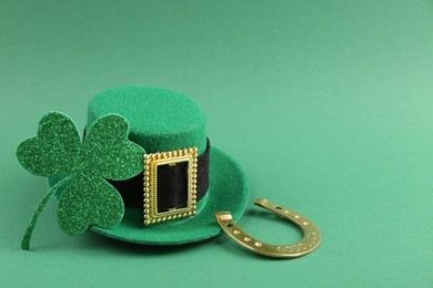 Photo of St. Patrick's day. Leprechaun hat, golden horseshoe and clover leaf on green background. Space for text