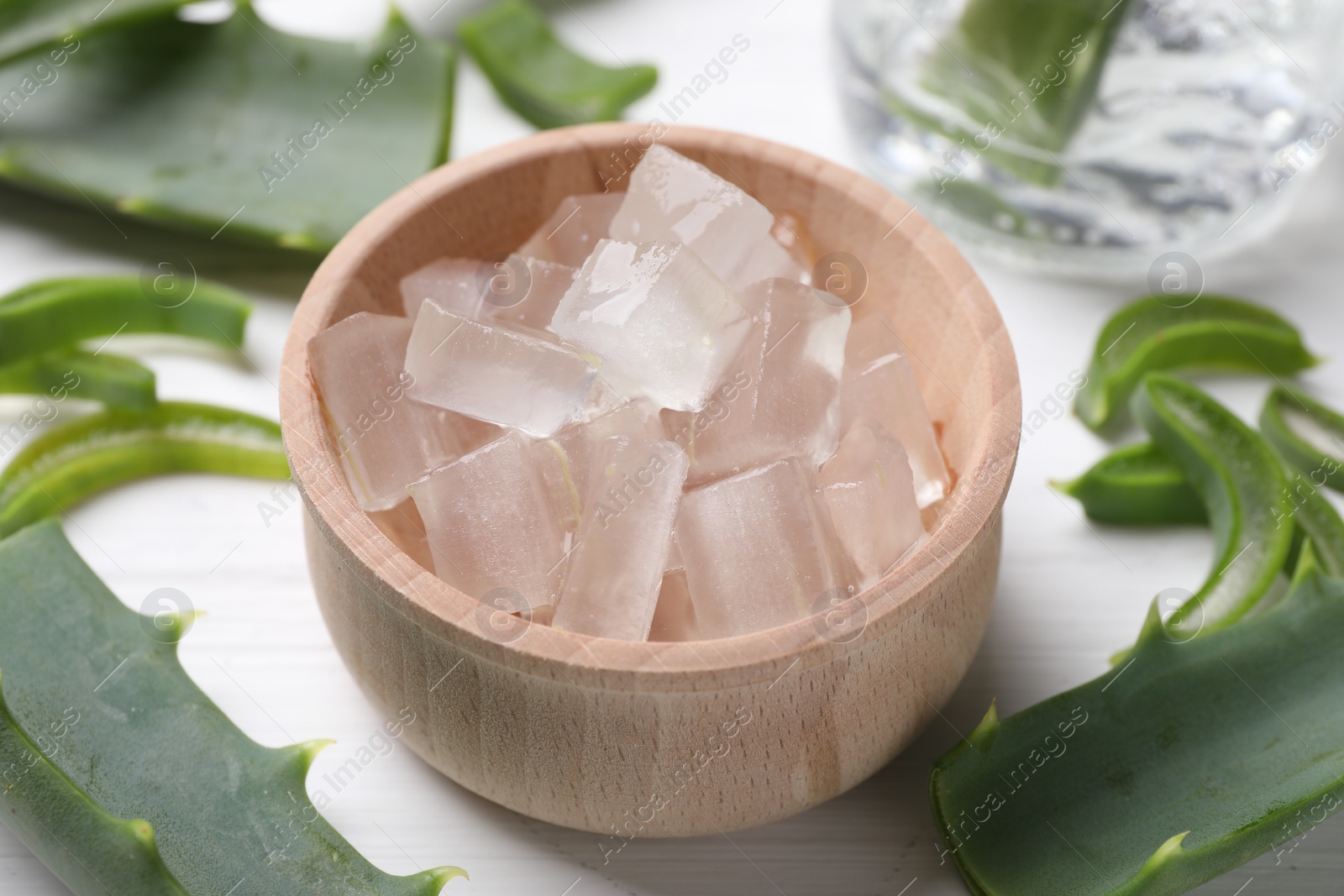 Photo of Aloe vera gel and slices of plant on white wooden table, closeup