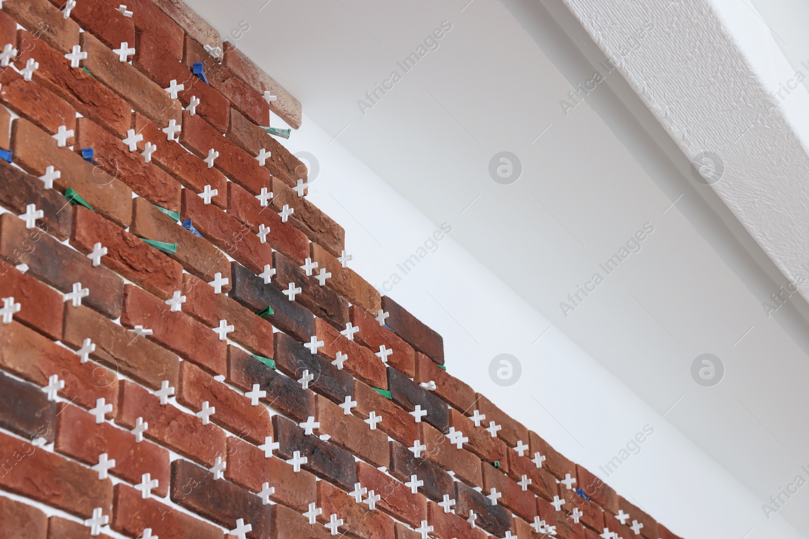 Photo of Decorative bricks with tile leveling system on white wall in repaired room