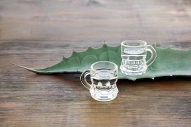 Photo of Mexican tequila shots and green leaf on wooden table. Drink made of agava