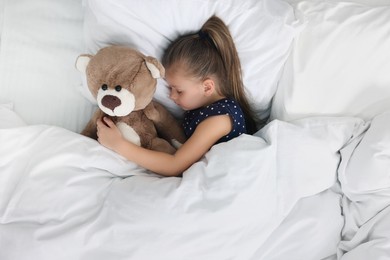 Photo of Cute little girl sleeping with teddy bear in bed, top view