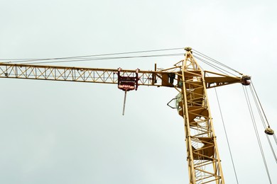 Photo of Tower crane under cloudy sky, low angle view. Construction site