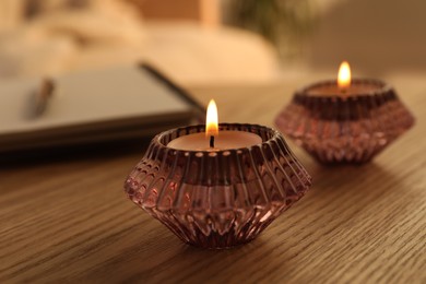 Photo of Burning candles in beautiful glass holders on wooden table indoors, closeup