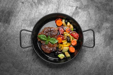 Photo of Pan with tasty steak and vegetables on grey table, top view