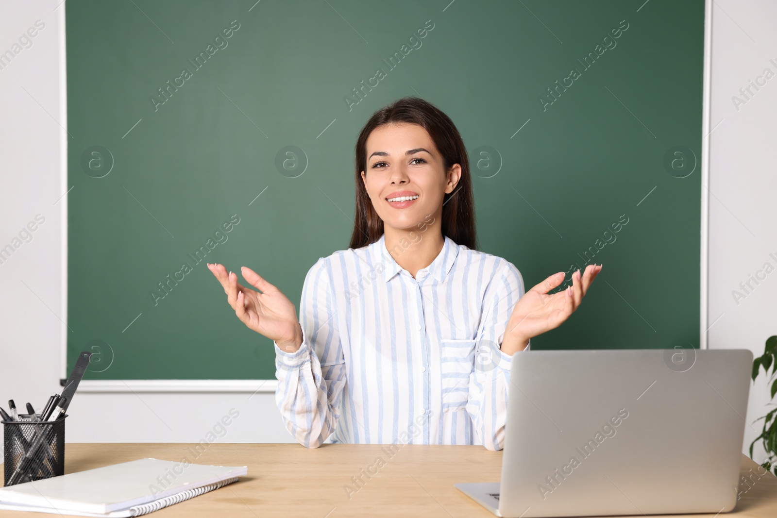 Photo of Happy young teacher explaining something at table in classroom