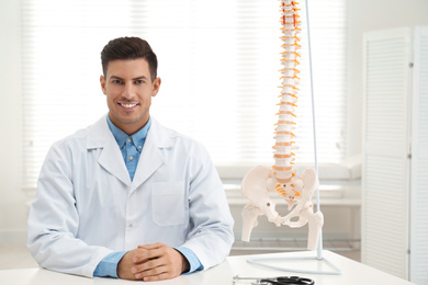 Male orthopedist at table near human spine model in office