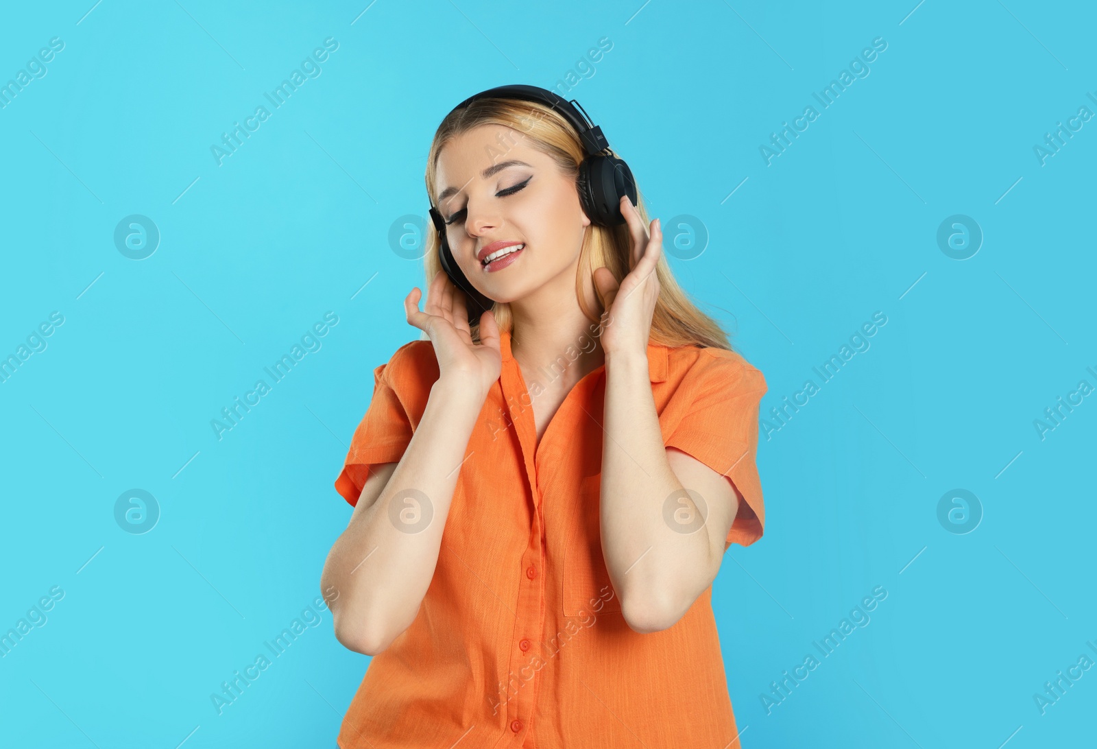 Photo of Happy woman in headphones enjoying music on light blue background