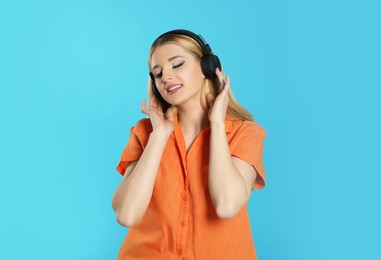 Photo of Happy woman in headphones enjoying music on light blue background