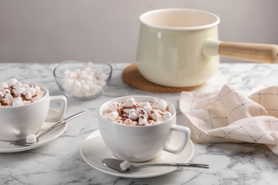 Photo of Aromatic hot chocolate with marshmallows and cocoa powder served on white marble table, closeup