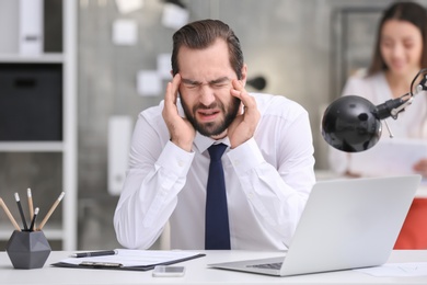 Photo of Young man suffering from headache in office