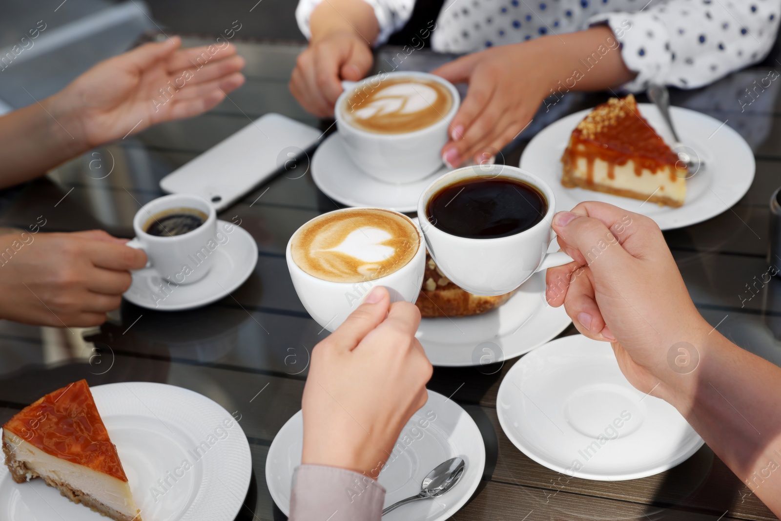 Photo of Friends drinking coffee at wooden table in outdoor cafe, closeup