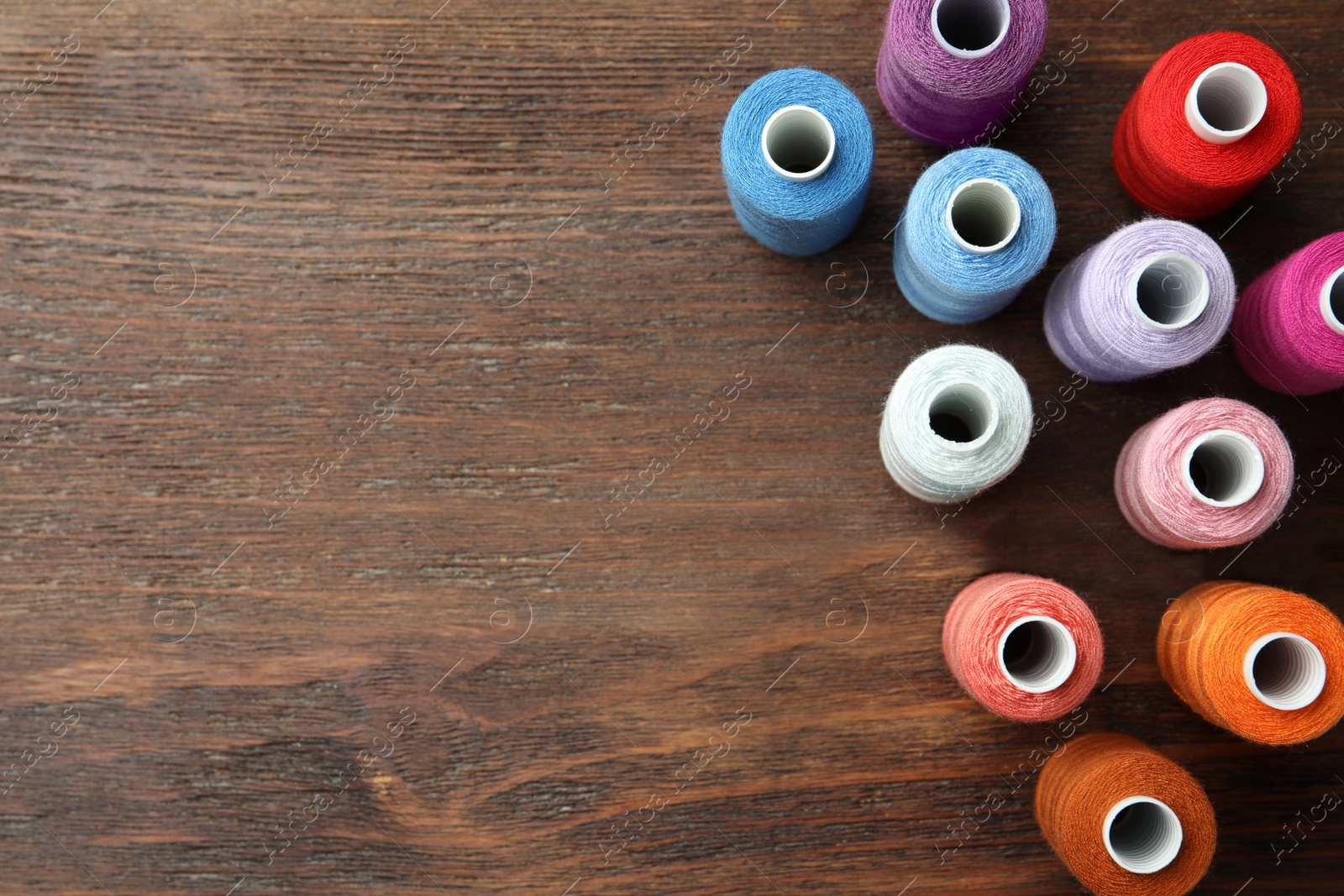 Photo of Set of colorful sewing threads on wooden table, flat lay. Space for text