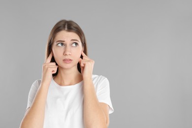 Photo of Emotional young woman covering her ears with fingers on grey background. Space for text