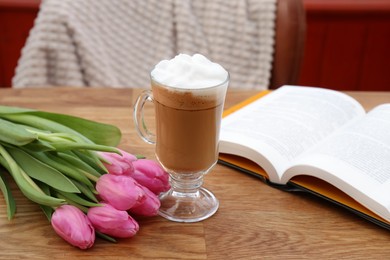 Glass of delicious cocoa, pink tulips and book on wooden table