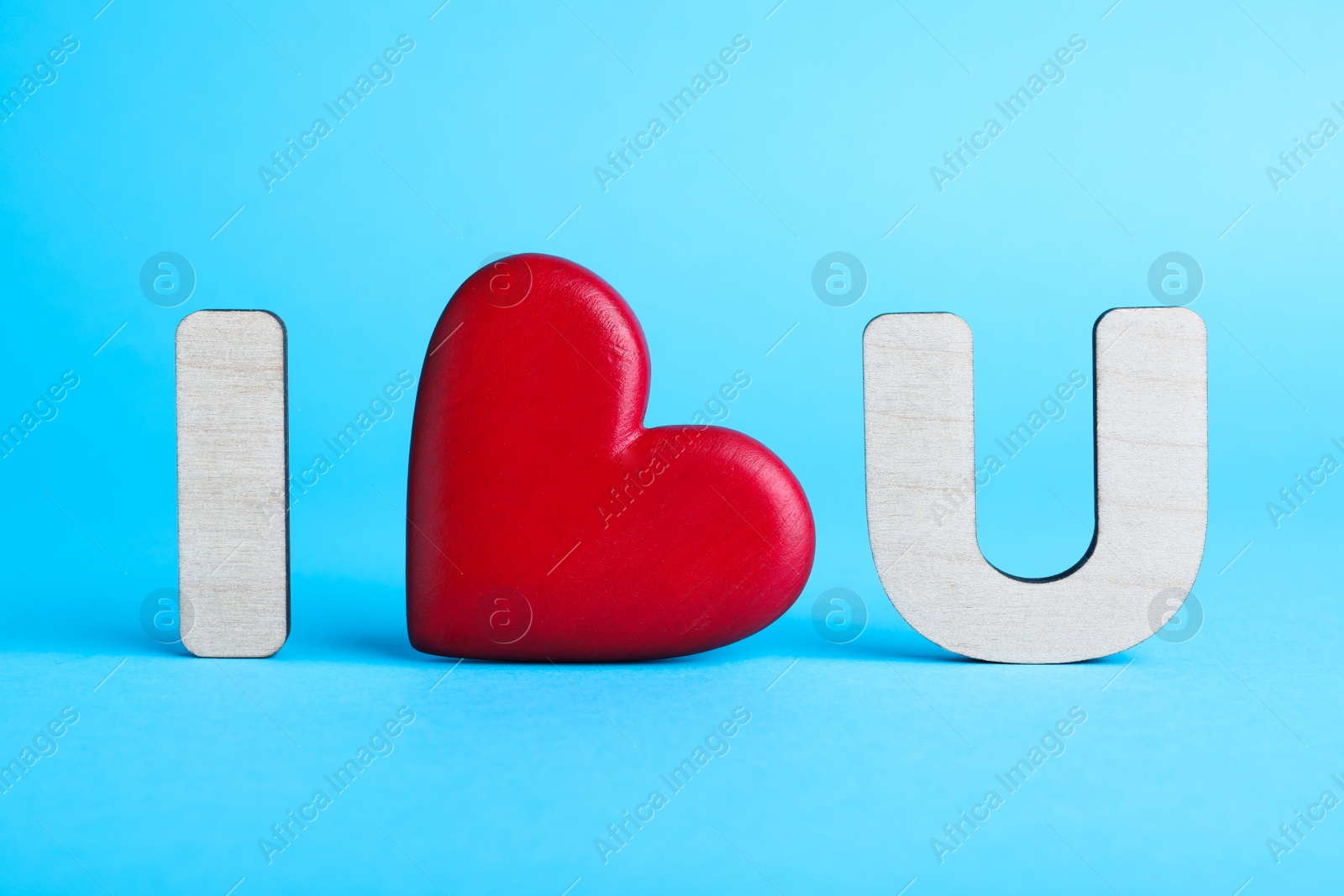 Photo of Phrase I Love You made of wooden letters and red heart on light blue background
