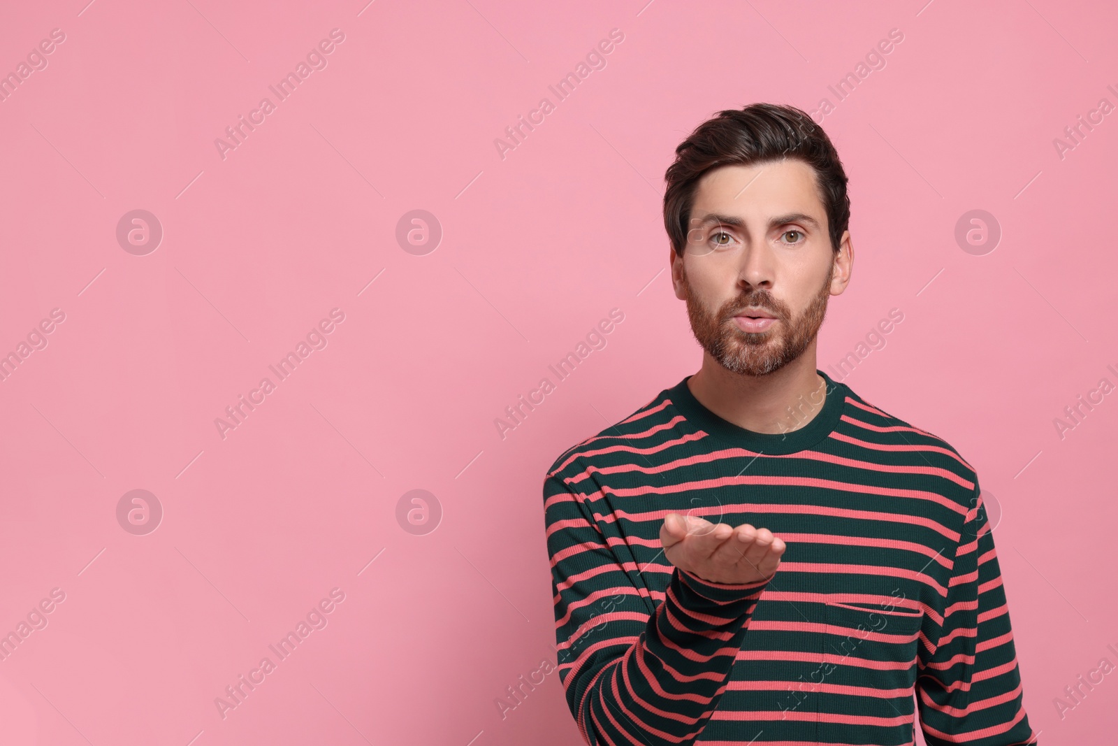 Photo of Handsome man blowing kiss on pink background. Space for text