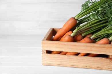 Ripe carrots in wooden crate on white table, closeup