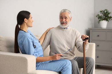 Photo of Health care and support. Nurse holding clipboard and laughing with elderly patient in hospital