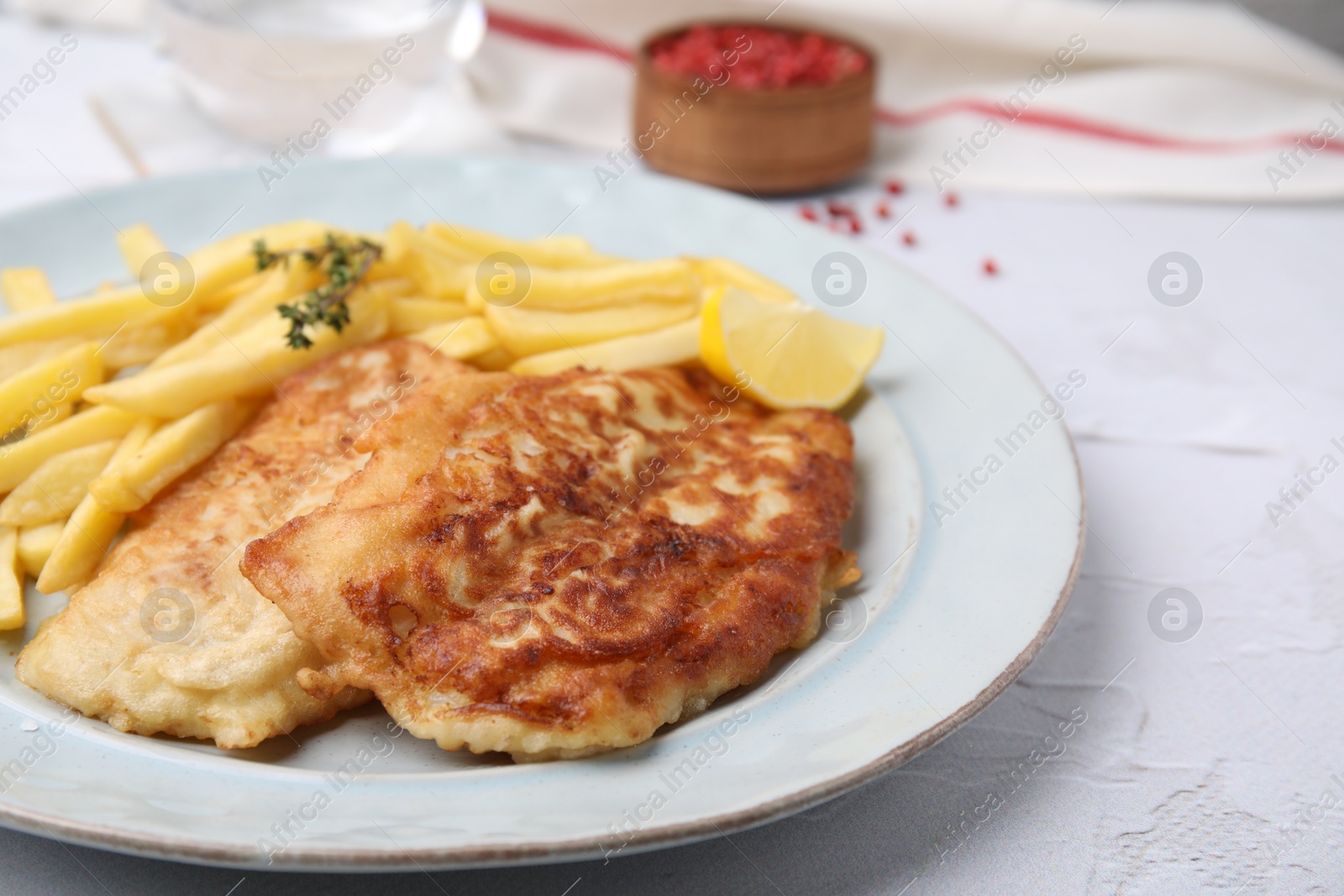 Photo of Tasty soda water battered fish, potato chips and lemon slice served on white textured table, closeup