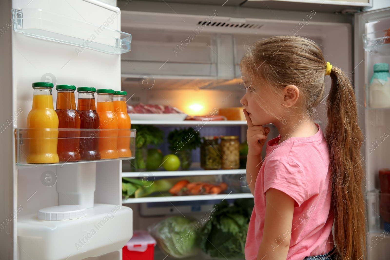 Photo of Cute little girl choosing food in refrigerator at home