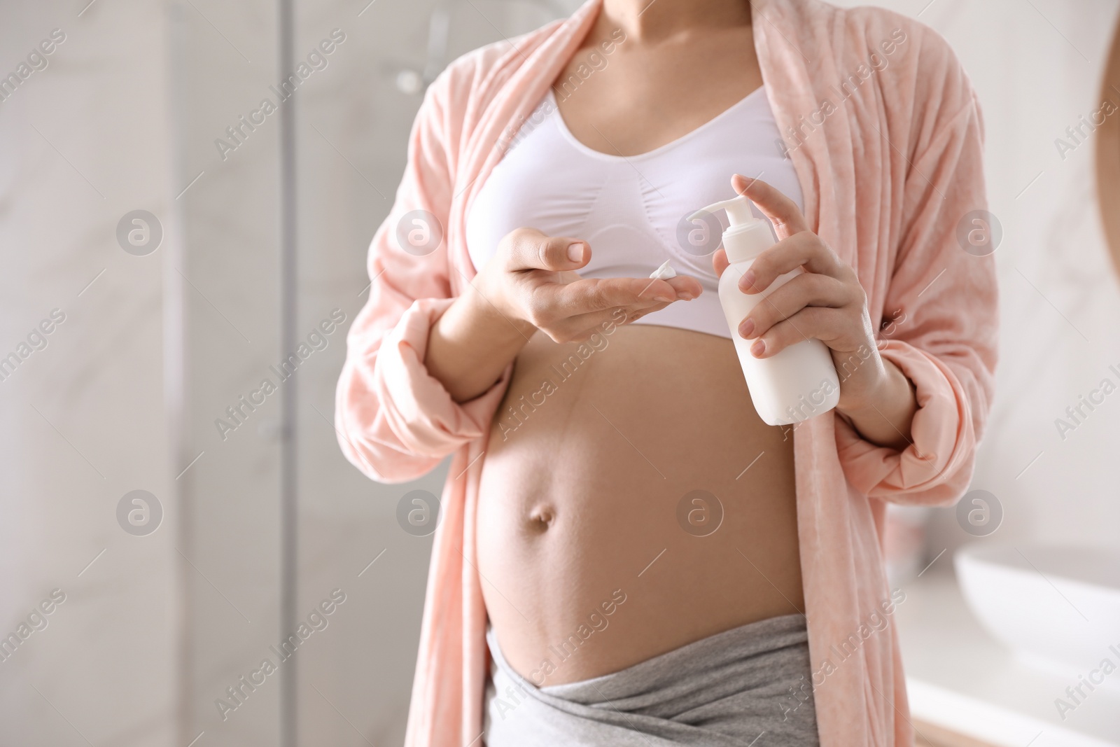 Photo of Young pregnant woman with cosmetic product in bathroom, closeup. Space for text