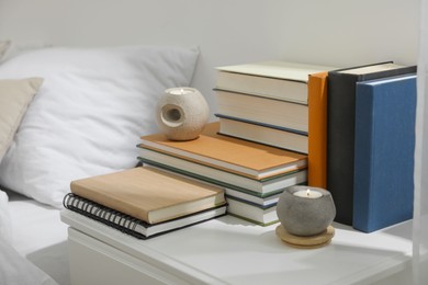 Hardcover books and scented candles on white bedside table indoors