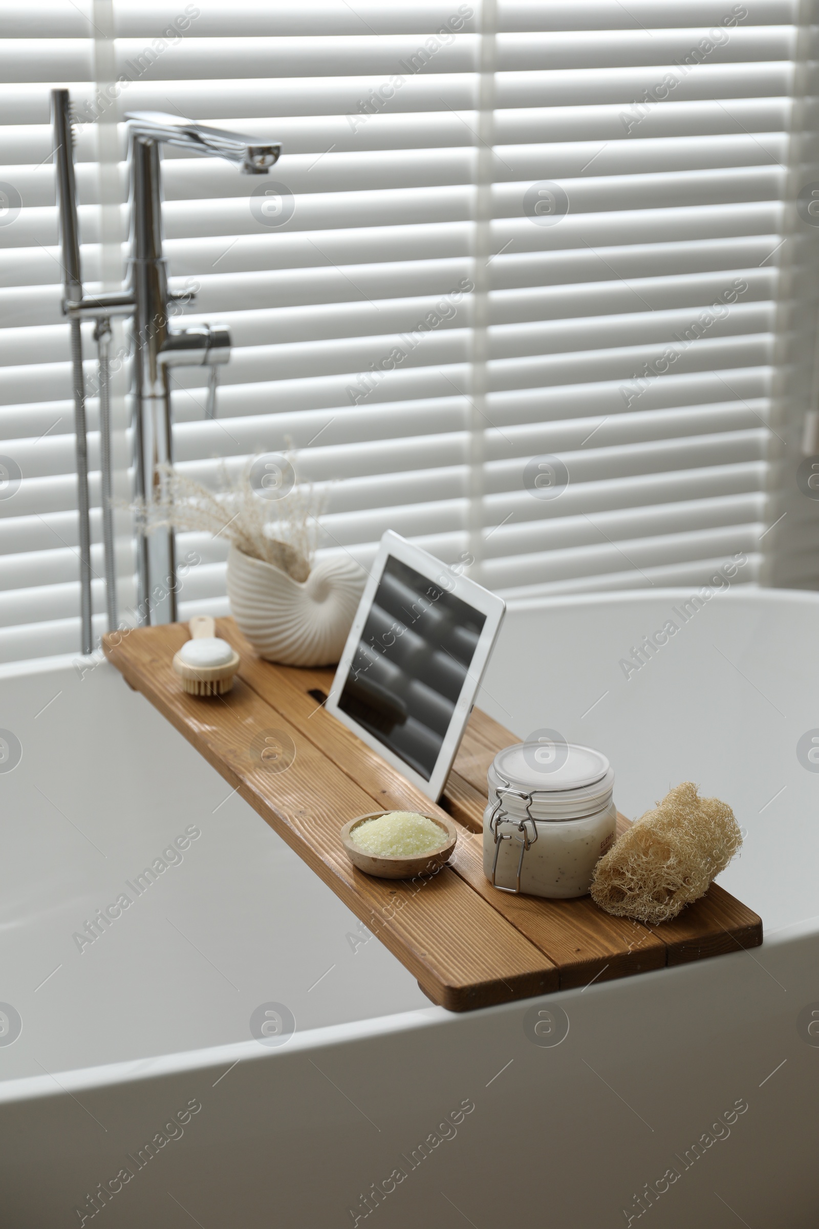 Photo of Wooden tray with tablet and spa products on bath tub in bathroom