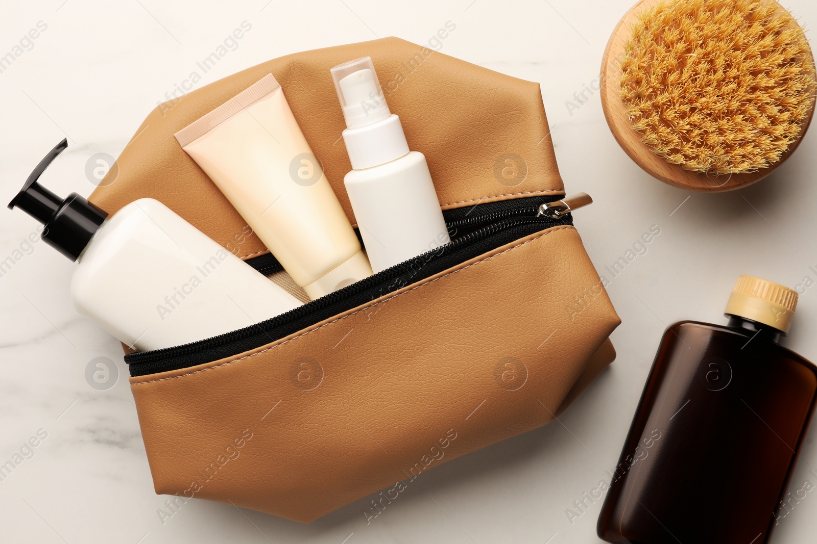 Photo of Preparation for spa. Compact toiletry bag and different cosmetic products on white marble table, flat lay