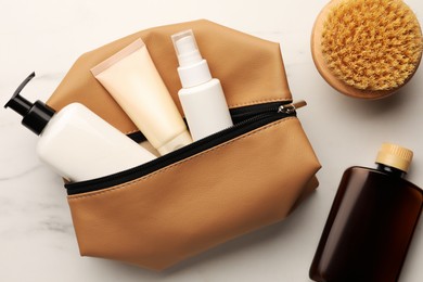 Photo of Preparation for spa. Compact toiletry bag and different cosmetic products on white marble table, flat lay