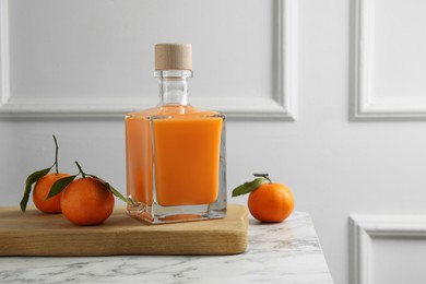 Delicious tangerine liqueur in bottle and fresh fruits on white marble table, space for text