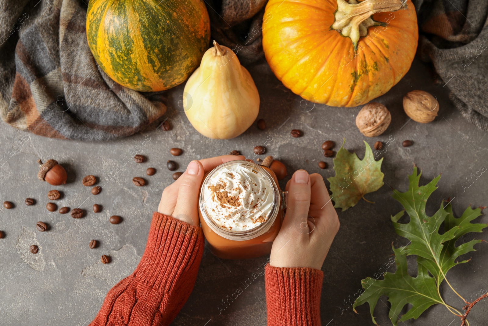 Photo of Woman holding mason jar of tasty pumpkin spice latte at grey table, top view