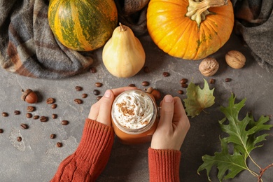 Woman holding mason jar of tasty pumpkin spice latte at grey table, top view